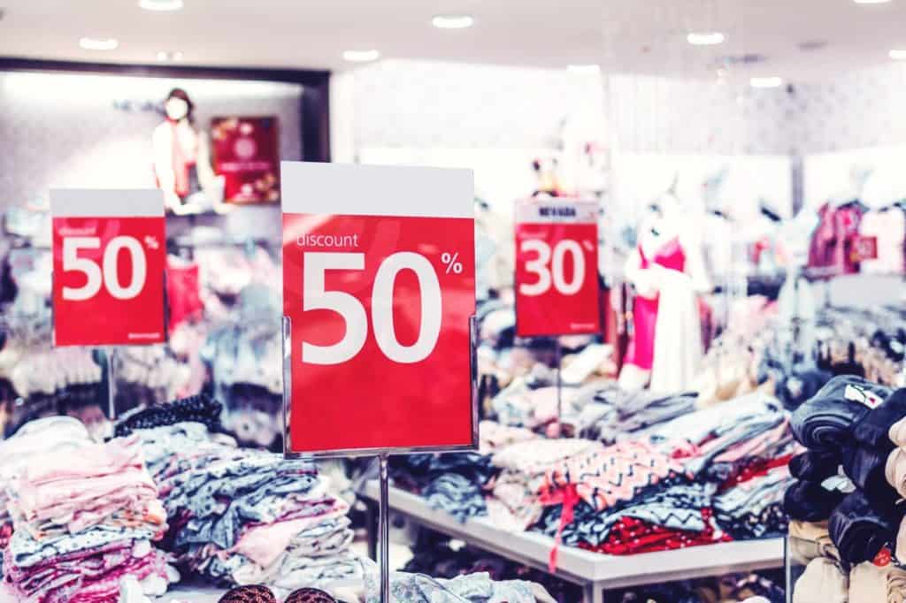 A discount sign hangs from a store window displaying items from a sale.
